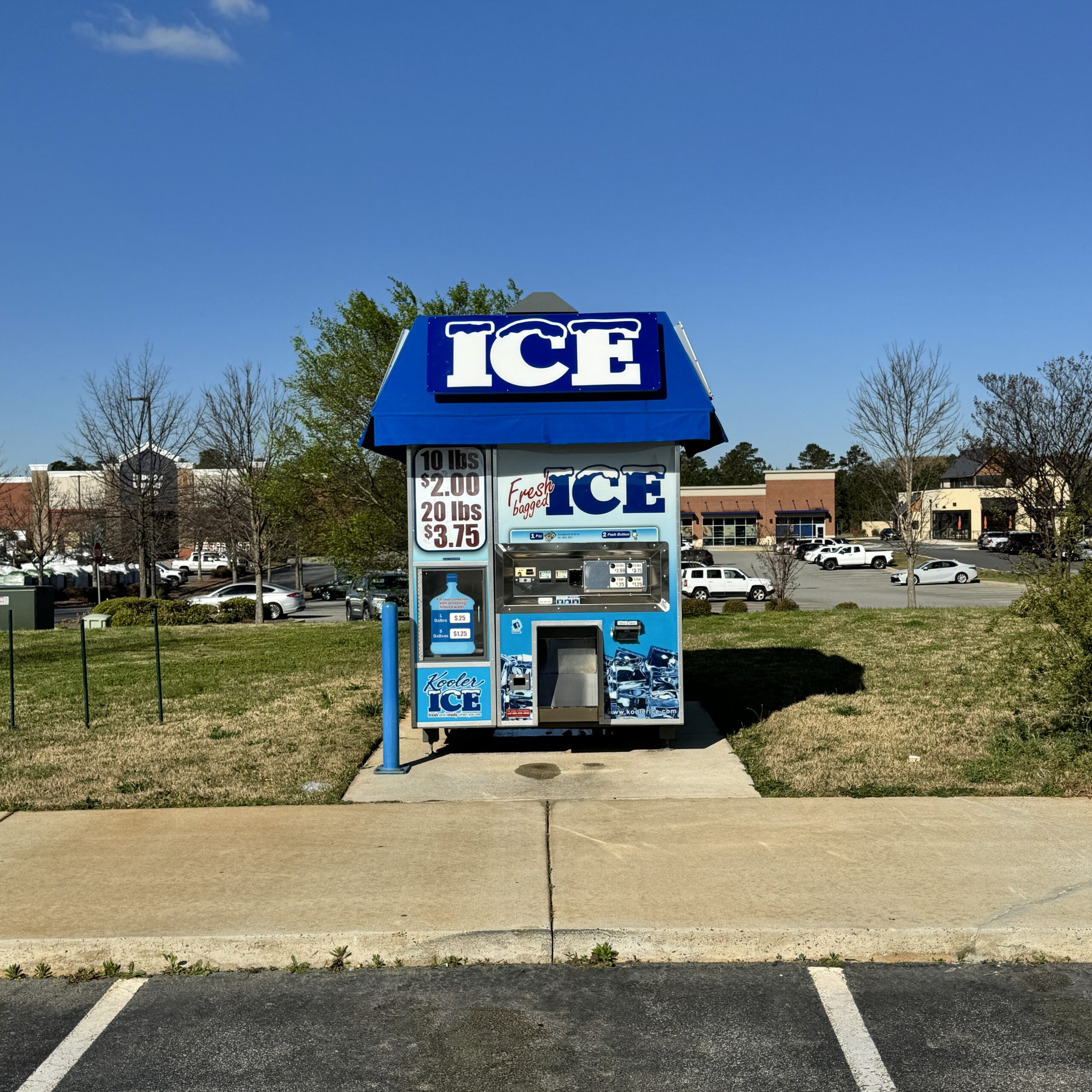 Blue ice vending cart with a large white ICE sign, set in a parking lot under a clear blue sky.
